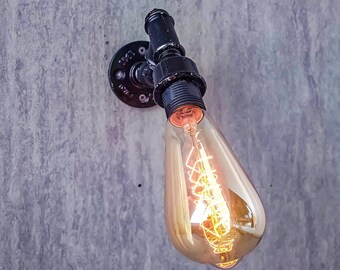 Könnte beinhalten: Ein schwarzer Metallrohranschluss mit einer durchsichtigen Glühbirne aus Glas. Die Glühbirne hat ein Filament, das bei eingeschaltetem Licht sichtbar ist.