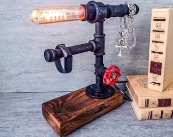 May include: A black metal pipe lamp with a red valve and a wooden base. The lamp has a clear glass bulb and a silver watch band holder. The lamp is sitting on a stack of books.