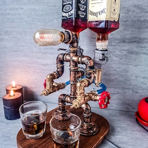 Puede incluir: Un dispensador de licor de estilo steampunk con dos botellas de Jack Daniel's, una con miel y la otra con whisky de Tennessee. El dispensador est&aacute; hecho de tuber&iacute;as y accesorios de cobre, y tiene dos vasos de vidrio llenos de l&iacute;quido. El dispensador est&aacute; sobre una base de madera y tiene una bombilla en la parte superior.