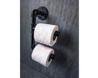 May include: Black metal double toilet roll holder mounted on a grey wall. Two rolls of toilet paper are on the holder.