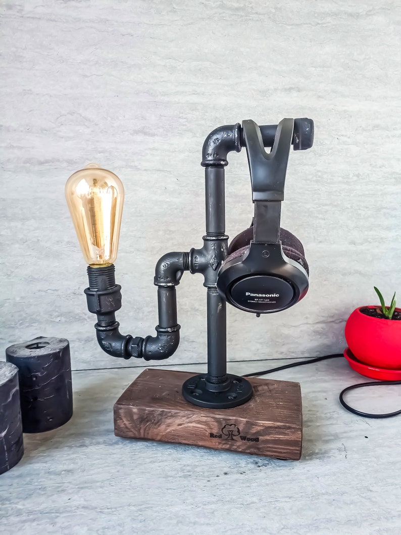 Puede incluir: Soporte de tuber&iacute;a de metal negro con una base de madera, que sostiene unos auriculares negros y una bombilla. La base est&aacute; grabada con "Red Wood".