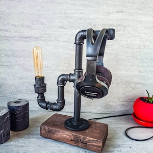 Puede incluir: Un soporte para auriculares de metal negro con una base de madera. El soporte est&aacute; hecho de tuber&iacute;as industriales y cuenta con una bombilla. La base est&aacute; grabada con "Red Wood".