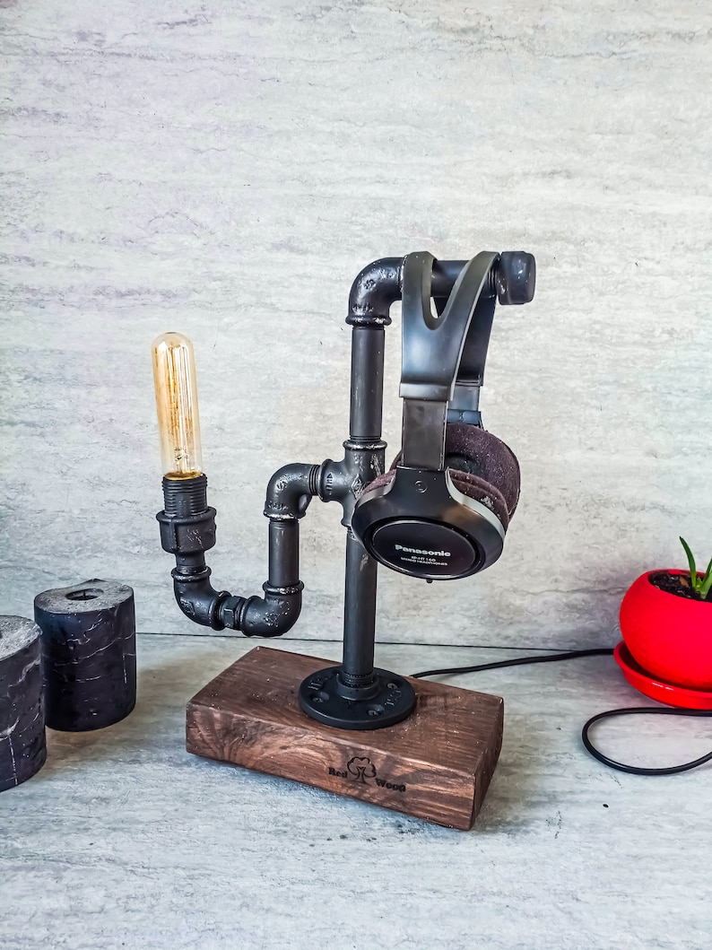 Puede incluir: Un soporte para auriculares de metal negro con una base de madera. El soporte est&aacute; hecho de tuber&iacute;as industriales y cuenta con una bombilla. La base est&aacute; grabada con "Red Wood".
