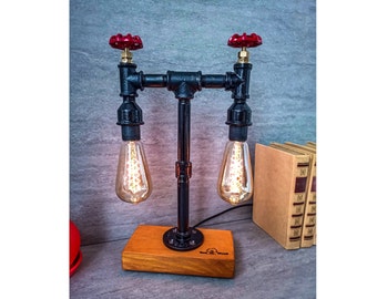 May include: A black metal table lamp with two Edison bulbs and red valve handles. The lamp has a wooden base and is plugged in with a black cord.