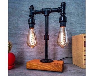 May include: A black metal table lamp with two Edison bulbs. The lamp is made of industrial pipe fittings and has a wooden base.