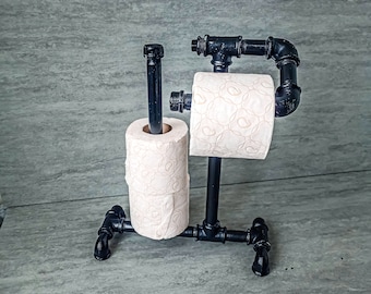 May include: Black metal toilet paper holder with two rolls of toilet paper. The holder is made of industrial pipe fittings.