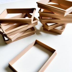 Puede incluir: Una pila de seis cortadores de galletas de plástico marrón en forma de rectángulo. Los cortadores de galletas están apilados uno encima del otro, siendo el cortador superior el más grande y el inferior el más pequeño.