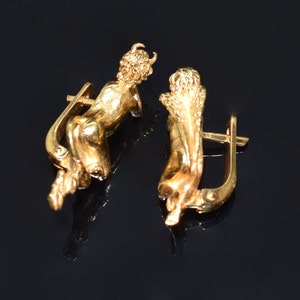 May include: A pair of gold-toned earrings featuring a cherub design. Each earring has a hook closure.