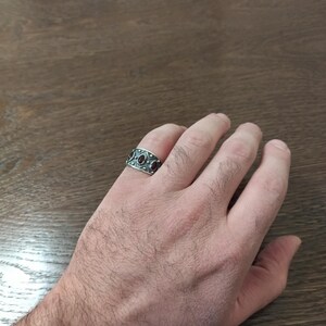 Pode incluir: Um anel de prata com uma banda larga e pedras preciosas vermelhas engastadas em um padr&atilde;o decorativo.