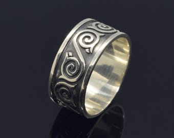 May include: A silver band ring with a wide band featuring a repeating pattern of stylized swirls.