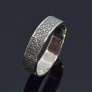May include: A silver band ring with a textured, geometric pattern. The ring is made of metal and has a polished finish.
