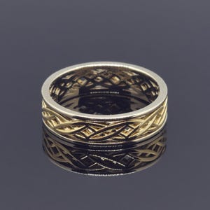 May include: A gold-toned ring with an intricate Celtic knot design. The ring features a band with interwoven patterns, creating a textured surface. The ring's design is visible both on the outer surface and the inner band, reflecting light and creating a detailed appearance.