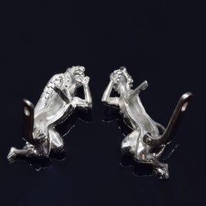 May include: A pair of silver angel earrings with detailed wings and a kneeling pose. The earrings have a post and butterfly back closure.