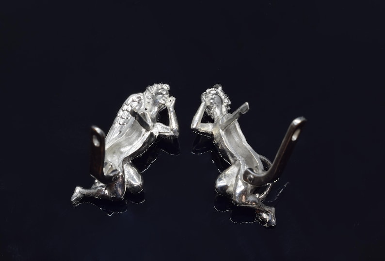 May include: A pair of silver angel earrings with detailed wings and a kneeling pose. The earrings have a post and butterfly back closure.