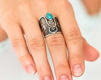 Puede incluir: Un anillo de plata con una piedra turquesa y diseños intrincados. El anillo es ancho y tiene una superficie texturizada.