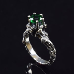 Puede incluir: Un anillo de plata con una piedra preciosa verde engastada en una banda retorcida con forma de rama.