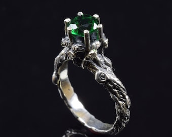 May include: A silver ring with a green gemstone set in a twisted, branch-like band.
