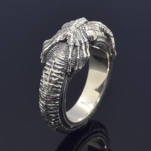 Peut inclure: Une bague en argent avec un design détaillé d'une créature aux griffes et au corps texturé.