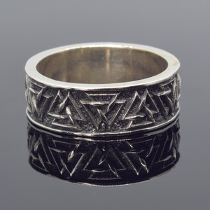 May include: A silver ring featuring a geometric pattern of triangles. The ring is wide and has a smooth, polished finish.