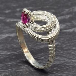 May include: A silver snake ring with a ruby-colored gemstone. The snake's head is open, revealing the gemstone. The ring is intricately detailed with a textured pattern, and the snake wraps around the finger.