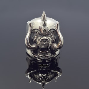 Könnte beinhalten: Ein silberner Ring mit einem detaillierten, aggressiven Wildschwein-Design. Der Ring hat eine stachelige Krone, große Stoßzähne und einen offenen Mund, was eine kühne Ästhetik erzeugt. Der Ring ist wahrscheinlich aus Metall und für einen auffälligen Look konzipiert.