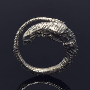 May include: A silver ring featuring a detailed sculpture of an alien creature in a curled position.