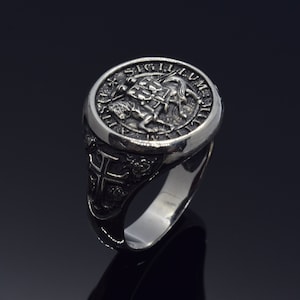 Könnte beinhalten: Ein silberner Ring mit einem detaillierten Design, das einen Ritter zu Pferd zeigt und die Inschrift "SIGILLUM MILITIAE TEMPLI" um den Rand.