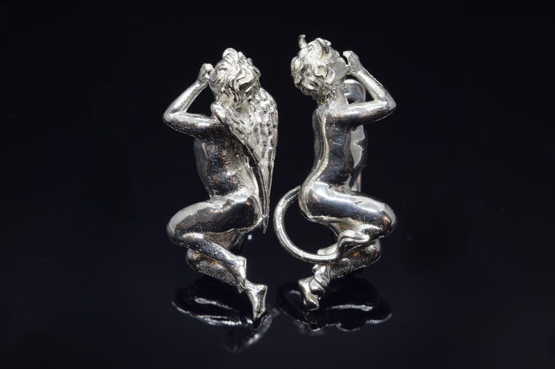 May include: A pair of silver cherub figurines with wings. The cherubs are facing each other and have their hands raised to their faces.