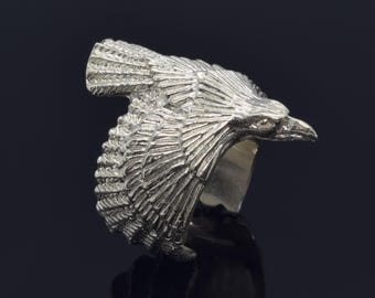 Könnte beinhalten: Ein silberner Ring mit einem detaillierten Adler-Design. Die Flügel des Adlers sind ausgebreitet und sein Kopf ist zur Seite gedreht. Der Ring ist aus Metall und hat eine glatte Oberfläche.