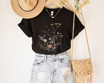 May include: A black t-shirt with a floral print of pressed flowers. The shirt is styled with a straw hat, denim shorts, and a woven bag.