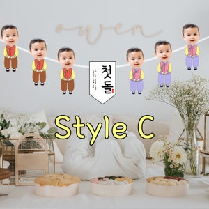 May include: A colorful banner with photos of babies in traditional Korean clothing. The banner has the text "첫돌" in Korean, which means "first birthday".