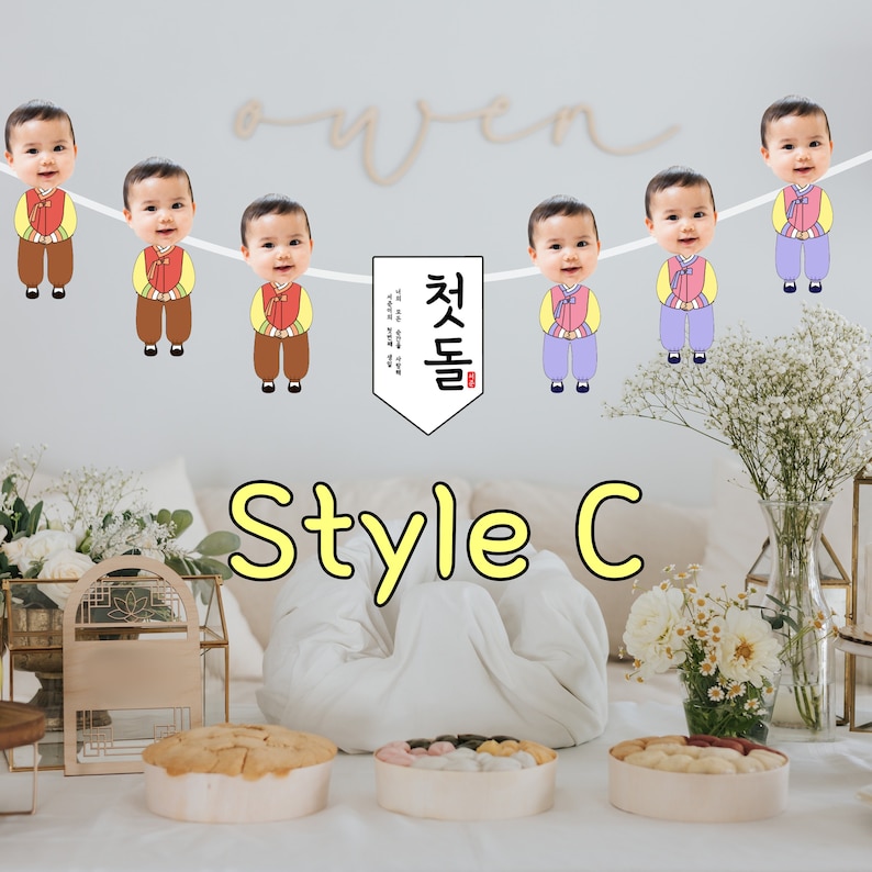 May include: A colorful banner with photos of babies in traditional Korean clothing. The banner has the text "첫돌" in Korean, which means "first birthday".