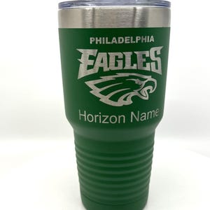 Pu&ograve; includere: Un bicchiere in acciaio inossidabile verde con coperchio trasparente, caratterizzato dal logo dei Philadelphia Eagles inciso in argento. Il testo PHILADELPHIA EAGLES &egrave; posizionato sopra l'emblema dell'aquila, con il testo Horizon Name inciso sotto.