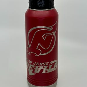 May include: Red stainless steel water bottle with a silver New Jersey Devils logo and the words "New Jersey Devils".