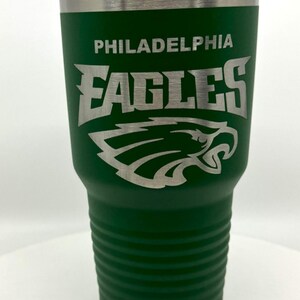 Pu&ograve; includere: Un bicchiere in acciaio inossidabile verde bosco con coperchio in plastica trasparente e il logo e il nome Philadelphia Eagles incisi in argento. Il bicchiere presenta una base scanalata testurizzata e una parte superiore liscia con bordo metallico.
