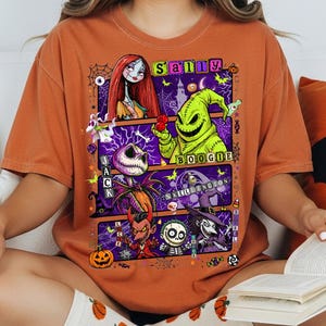 May include: A burnt orange short-sleeve t-shirt featuring a graphic print of characters from The Nightmare Before Christmas, including Sally, Jack Skellington, and Oogie Boogie, with text labels for each character and a purple background.