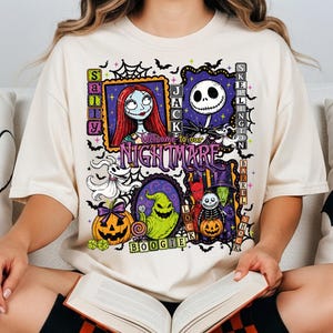 May include: A cream-colored t-shirt featuring a graphic print of characters from The Nightmare Before Christmas, including Jack Skellington, Sally, and Oogie Boogie. The design includes the text Welcome to our NIGHTMARE and various Halloween-themed motifs like pumpkins, bats, and spiderwebs.