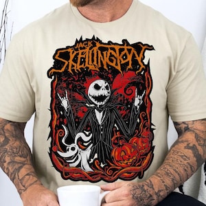 May include: Beige t-shirt featuring a graphic of Jack Skellington from The Nightmare Before Christmas. The design includes Jack, pumpkins, and the text "Jack Skellington" in a stylized font. The shirt is a crew neck.