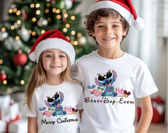 May include: Two children wearing white t-shirts with a cartoon character design and Santa hats. The shirts feature the character Stitch decorated with Christmas lights and the phrases "Merry Christmas" and "Best Day Ever". A Christmas tree is in the background.