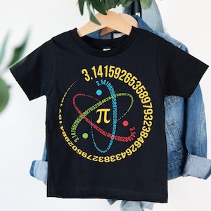 May include: Black t-shirt with a colorful graphic design featuring the mathematical symbol Pi and the digits of Pi. The design includes a yellow Pi symbol, and the numbers are arranged in a circular pattern. The shirt is hanging on a wooden hanger.