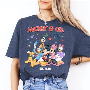 A woman wearing a blue t-shirt with a graphic of Disney characters and text.