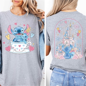 The image is a collage of two photos featuring a gray t-shirt with a cartoon character and a castle. The front photo shows the character sitting in a teacup, surrounded by hearts and flowers, while the back photo shows the same character standing in front of a castle.