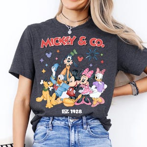 A woman wearing a gray t-shirt with a graphic of Disney characters Mickey Mouse and Donald Duck, along with the text "Mickey & Co." and "Est. 1928".