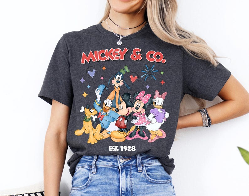 A woman wearing a gray t-shirt with a graphic of Disney characters Mickey Mouse and Donald Duck, along with the text "Mickey & Co." and "Est. 1928".