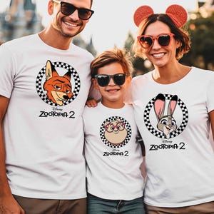 A man, a woman, and a child wearing white t-shirts with Disney characters printed on them, smiling and posing together.