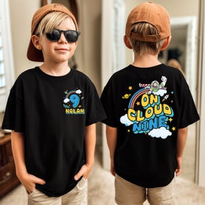 A young boy wearing a black t-shirt with a graphic design on the back, including a character and the text "ON CLOUD NINE".