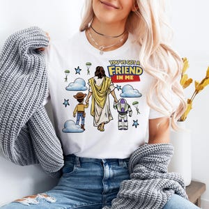 A woman wearing a white t-shirt with a graphic design of a cartoon character and text, along with a gray sweater and blue jeans.