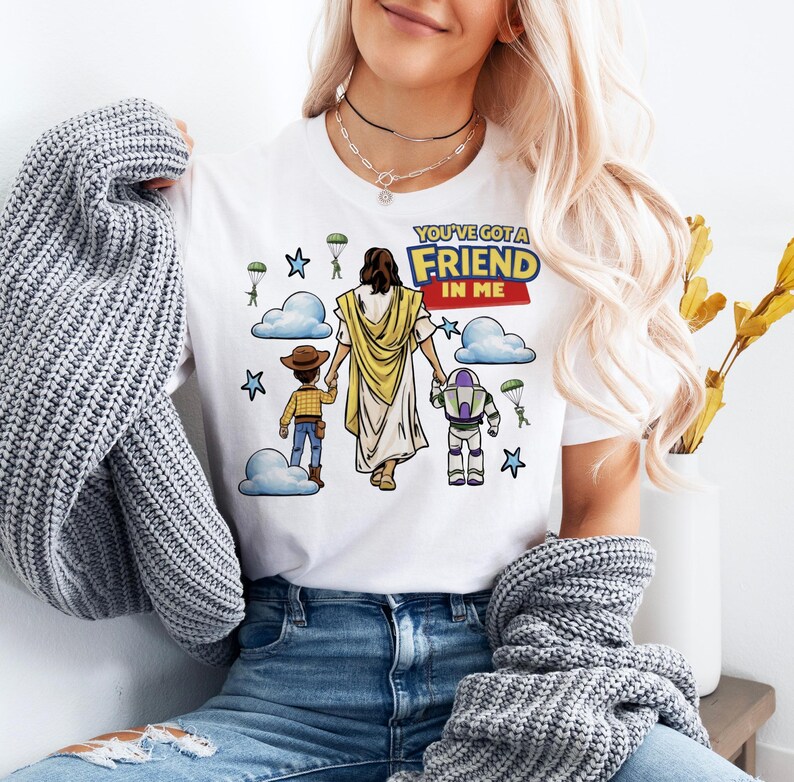 A woman wearing a white t-shirt with a graphic design of a cartoon character and text, along with a gray sweater and blue jeans.