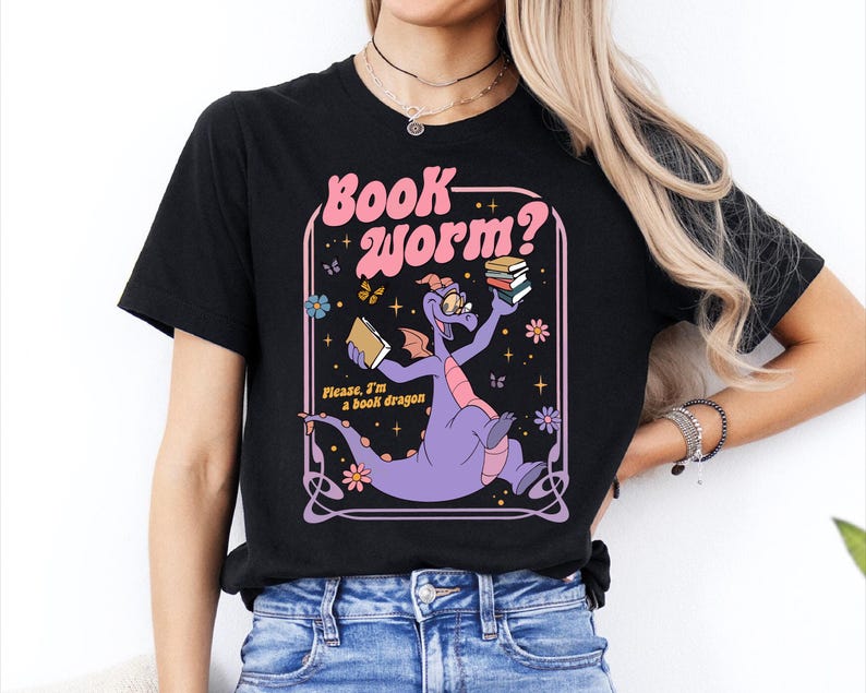 A woman wearing a black t-shirt with a graphic design featuring a purple dragon holding books and surrounded by stars and flowers.
