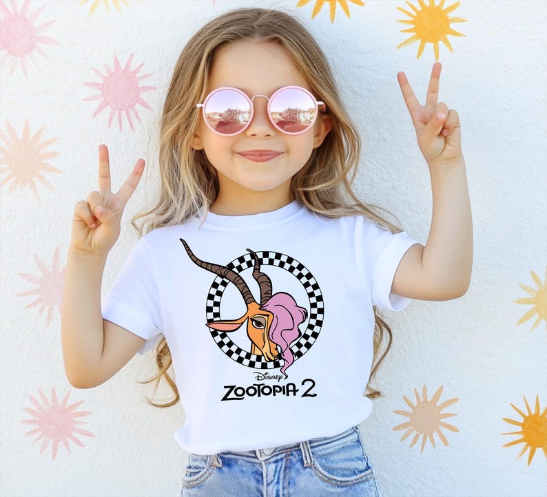 A young girl wearing a white t-shirt with a graphic of a cartoon character and pink sunglasses is making a peace sign with her hands.